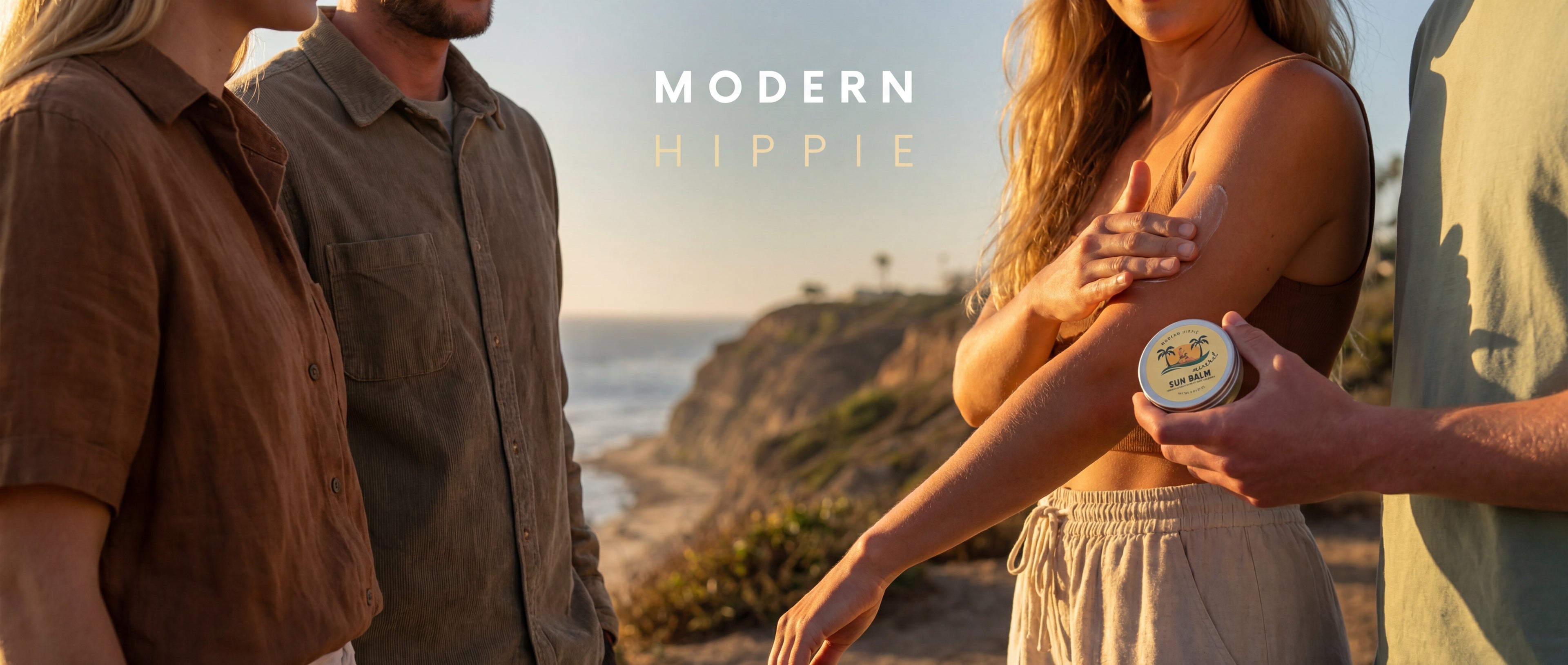 Four people standing on a cliff near a beach with a scenic background, holding a sunscreen product labeled 'Modern Hippie'.